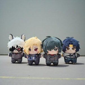 Könnte beinhalten: Vier Plüschpuppen mit Charakterdesigns im Anime-Stil. Jede Puppe hat eine einzigartige Frisur und Kleidung, mit detaillierten Gesichtszügen und kleinen Körpern. Die Puppen stehen in einer Reihe vor einem schlichten Hintergrund.