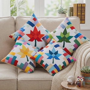 May include: Four square throw pillows with a white background and a colorful maple leaf design. The leaves are red, green, yellow, and blue. The borders of the pillows are made of colorful patchwork fabric. The pillows are on a beige sofa.