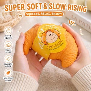 May include: An orange croissant-shaped stress relief toy is held in two hands. The toy has a yellow label with a cartoon croissant and the text "CROISSANT - Fun and interesting." The image also includes text that says "SUPER SOFT & SLOW RISING" and "SQUEEZE, RELAX, ENJOY!"