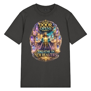 May include: A charcoal grey short-sleeved t-shirt featuring a central graphic of a figure with arms outstretched surrounded by glowing portals. The text reads: EVERY DOOR OPENS WHEN I BREATHE IN NEW REALITIES, set against a vibrant, cosmic background.