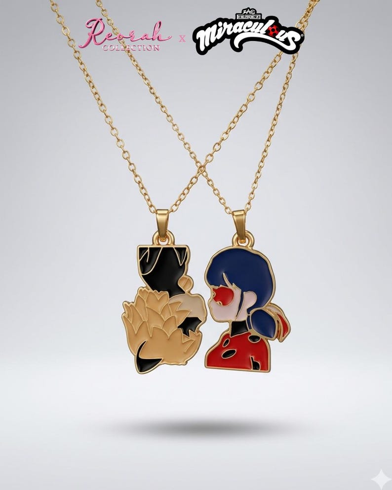 May include: A gold-toned necklace set featuring two pendants that form a pair. One pendant depicts a black and tan fox-like character, while the other shows a character with dark blue hair and a red, black-spotted suit. Text reads Reorah x Miraculous.
