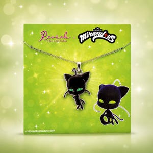 May include: A silver-toned metal necklace featuring a black enamel pendant shaped like a stylized cat-like creature with bright green eyes. The pendant is displayed on a green card with the text Reorah Collection and Miraculous.