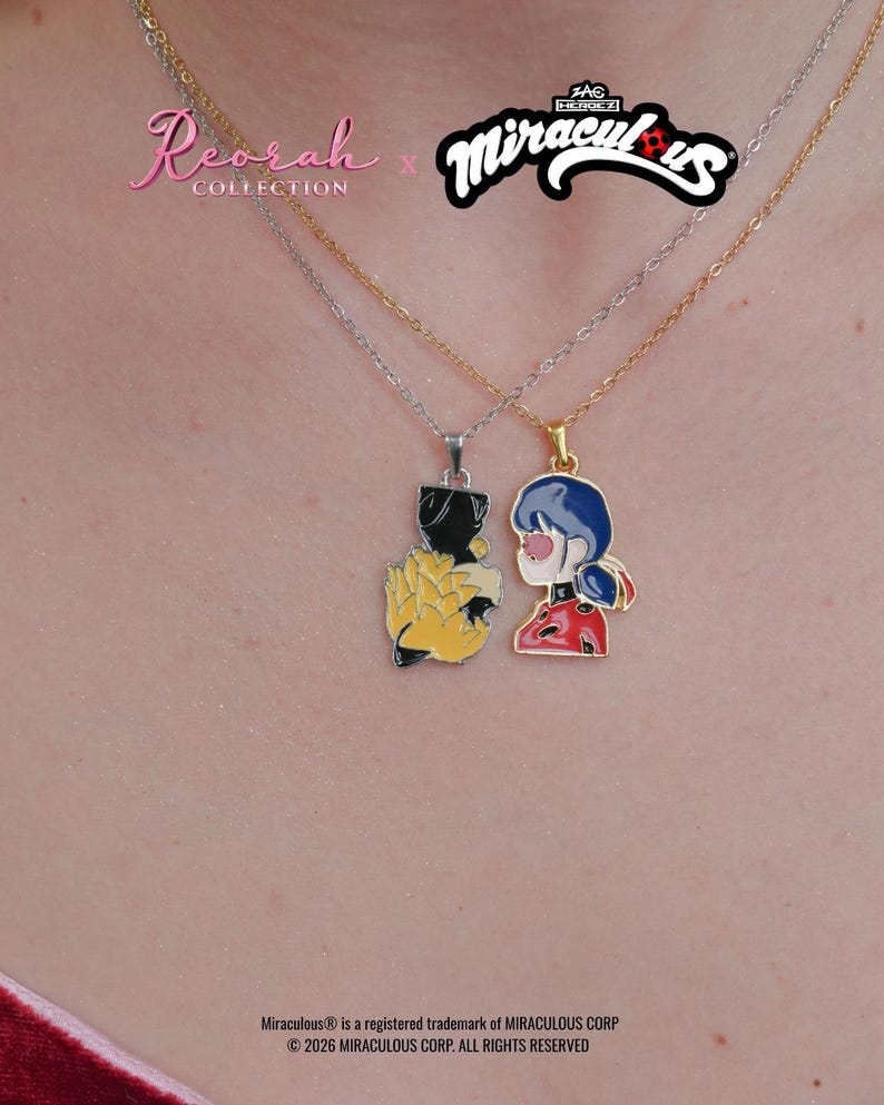 May include: Two necklaces from the Reorah Collection x Miraculous collaboration. One silver-tone chain features a black and yellow pendant, while the gold-tone chain features a pendant depicting a character with blue hair in a red and black outfit.