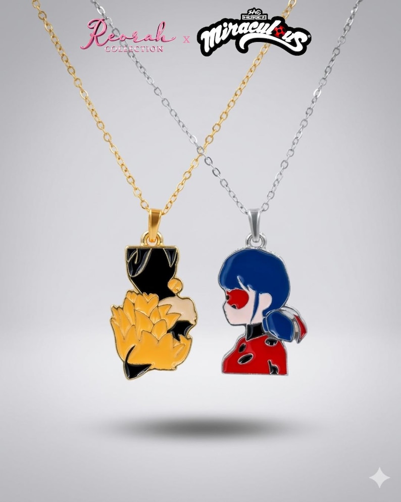 May include: Two necklaces featuring enamel pendants from the Reorah Collection x Miraculous collaboration. One gold-toned chain holds a black and yellow fox-themed pendant, while the silver-toned chain holds a red, blue, and black Ladybug character pendant.