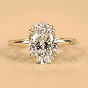 Puede incluir: Un anillo de oro con una gran piedra preciosa transparente de talla ovalada, sujeta por un engaste de múltiples garras. La banda es fina, pulida y de oro macizo, lo que proporciona un aspecto limpio y clásico a esta pieza de joyería.