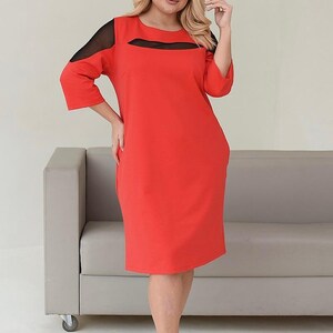 May include: A knee-length, red dress with three-quarter sleeves and black mesh accents at the shoulders and neckline. The dress has a simple, elegant design, suitable for various occasions. The model is wearing black heels.