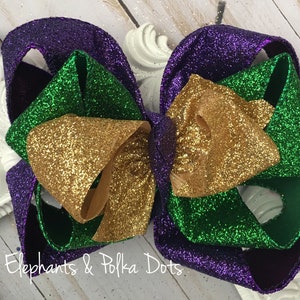 May include: A large purple, green, and gold glitter bow. The bow is made of three layers of ribbon, each with a different color of glitter.