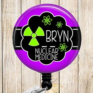 May include: Purple and black badge reel with a green radiation symbol, the text "BRYN - NUCLEAR MEDICINE" and a black and white stripe.