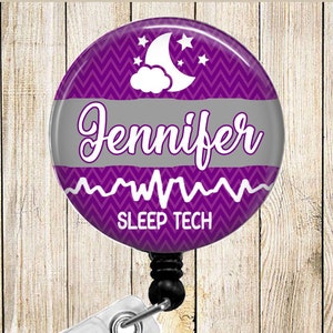 May include: A purple and gray retractable badge reel with the name "Jennifer" in script. The design includes a chevron pattern, a moon and stars, and the words "SLEEP TECH". The reel has a white clip.