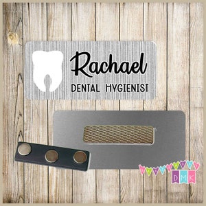 May include: A silver name tag with a white tooth icon and the text "Rachael Dental Hygienist" in black lettering.