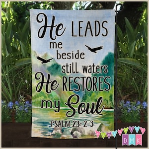 Peut inclure: Un drapeau de jardin en aquarelle avec un ciel bleu, des arbres verts et une rivière. Le drapeau présente le texte "He Leads me beside still waters He Restores my Soul Psalm 23:2-3".