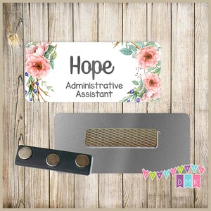 May include: A white name tag with a floral design and the text "Hope Administrative Assistant". The name tag is attached to a silver magnetic name tag holder.