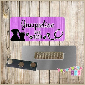 May include: Purple and white striped name tag with the text "Jacqueline Vet Tech" and a black silhouette of a dog and cat. The name tag is attached to a silver magnetic name tag holder.