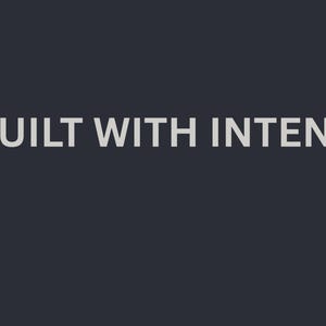 Può includere: La frase "BUILT WITH INTENT" è visualizzata in grigio chiaro, con un carattere sans-serif, su uno sfondo grigio scuro. Il testo è centrato e occupa una parte significativa dell'immagine.