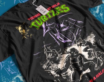 May include: Black t-shirt with a graphic of the Teenage Mutant Ninja Turtles. The design includes the words "Teenage Mutant Ninja Turtles" in green and purple, and "Heroes in a Half Shell" in pink. A tag reads "Large".