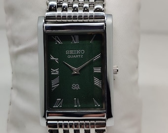 May include: A rectangular Seiko Quartz watch with a dark green dial, silver-tone Roman numeral hour markers, and silver hands. The watch features a polished silver-tone metal case and a multi-link stainless steel bracelet with a textured finish.