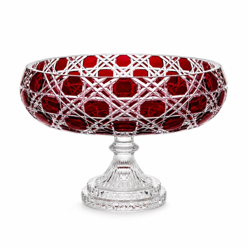 May include: A deep red crystal bowl with a clear glass pedestal base. The bowl features a complex cut-glass pattern of intersecting lines and hexagonal shapes. The clear glass stem and circular base have a vertical ribbed texture and faceted edges.