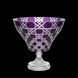 May include: A deep purple crystal bowl featuring intricate cross-hatched and diamond-cut patterns throughout the glass. The bowl sits on a clear, faceted pedestal base with a circular foot, showcasing a contrast between the colored glass and clear stem.