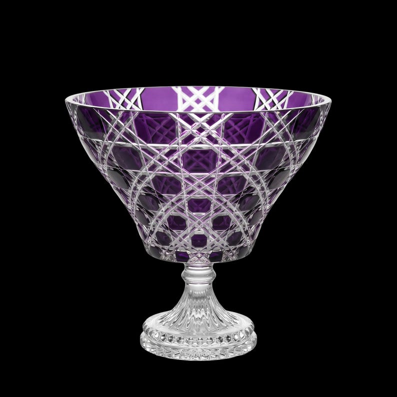 May include: A deep purple crystal bowl featuring intricate cross-hatched and diamond-cut patterns throughout the glass. The bowl sits on a clear, faceted pedestal base with a circular foot, showcasing a contrast between the colored glass and clear stem.