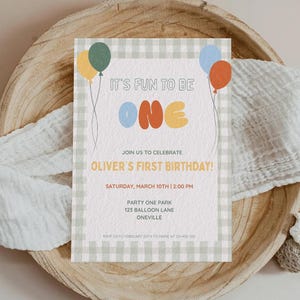 Könnte beinhalten: Eine Geburtstagseinladung mit einem grün-weißen Vichy-Rand. Der Text lautet "IT'S FUN TO BE ONE" mit bunten Luftballons. Die Einladung ist für Olivers ersten Geburtstag, mit Datum, Uhrzeit und Ortsangaben.