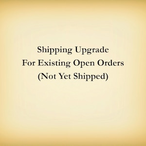 May include: A rectangular graphic with a light beige background featuring centered black text that reads: Shipping Upgrade For Existing Open Orders (Not Yet Shipped). The design has a subtle vignette effect with darker edges.