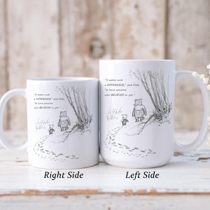 May include: Two white ceramic mugs with a black and white illustration of Winnie the Pooh and Piglet walking in a forest. The mugs have the quote, "It makes such a difference," and "to have someone who BELIEVES in you."