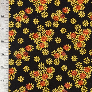 May include: Close-up of a black fabric with a repeating floral pattern. The design features clusters of yellow and orange daisy-like flowers. The flowers are evenly spaced across the dark background, creating a vibrant and cheerful textile.