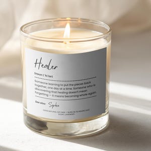 Puede incluir: Una vela en vaso de cristal transparente con una etiqueta blanca que muestra el texto Healer, una definición de la palabra y el nombre Sophia. La vela contiene cera color crema, una mecha encendida y 100% cera de soja natural, 312g, aroma lavanda.