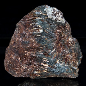 May include: A raw mineral specimen featuring a dense cluster of fibrous, metallic, reddish-brown and dark gray crystals. The structure displays a radiating, needle-like texture with a small, distinct patch of white, crystalline material at the top.