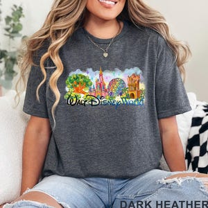 May include: A dark heather gray short-sleeve t-shirt featuring a colorful graphic of the Walt Disney World theme park landmarks, including a tree, a castle, a geodesic sphere, and a tower, with the text Walt Disney World printed in blue.