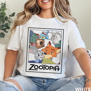 May include: White t-shirt featuring a graphic from the animated movie Zootopia. The graphic includes characters like Judy Hopps and Nick Wilde. The word "Zootopia" is printed in a bold, black font. The shirt is made of a soft material.