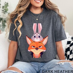 May include: Dark heather gray t-shirt featuring a cartoon image of a fox and a bunny. The fox is orange and the bunny is gray. The text "DARK HEATHER" is printed at the bottom of the shirt.