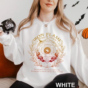 May include: White sweatshirt with a circular graphic that reads "IRON FLAME BURN IT DOWN" in gold and red. The design includes a bird emblem and floral elements. Below the graphic is text. The word "WHITE" is printed at the bottom.