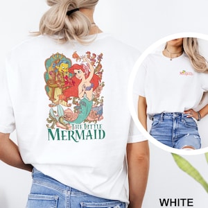 May include: White t-shirt featuring a colorful graphic of Ariel from The Little Mermaid, with the text "The Little Mermaid" in green. The shirt also has a small "Mermaid" text on the front.