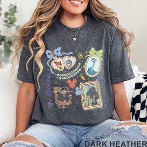 Puede incluir: Camiseta gris jaspeado oscuro con personajes de Zootopia en ilustraciones enmarcadas. La camiseta incluye im&aacute;genes de Nick Wilde, Judy Hopps y otros personajes. El texto "Zootopia" est&aacute; impreso verticalmente en el lado izquierdo. Las palabras "Dark Heather" est&aacute;n impresas en la parte inferior.