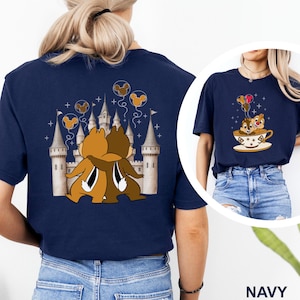 May include: Navy blue t-shirt featuring a cartoon illustration of Chip and Dale hugging in front of a castle. The design includes Mickey Mouse balloons and stars. A smaller image on the right shows Chip and Dale in a teacup with balloons.