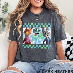 May include: Dark heather gray t-shirt featuring a graphic of three cartoon characters: a fox, a snake, and a rabbit. The graphic is framed with a checkered pattern in blue and green. The text "DARK HEATHER" is printed at the bottom.