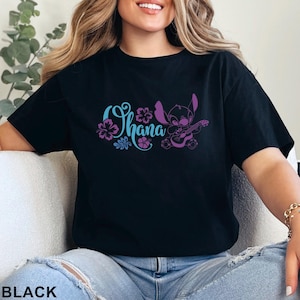 May include: Black t-shirt featuring the word "Ohana" in teal and purple floral design, with a purple cartoon character playing a ukulele. The word "BLACK" is printed at the bottom of the shirt.