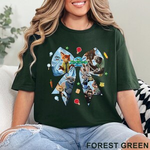 Op de afbeelding: Bosgroen T-shirt met een groot strikdesign met personages uit de animatiefilm "Zootopia". De strik is gevuld met afbeeldingen van de personages en het woord "Zootopia" staat in het midden gedrukt. Het shirt is effen van kleur.