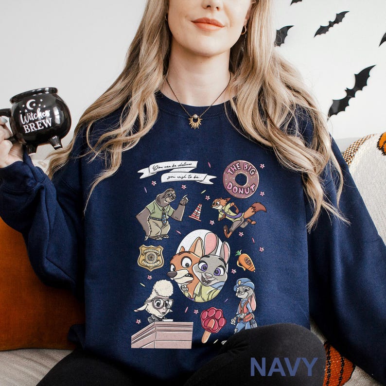 May include: Navy blue sweatshirt featuring a colorful graphic of characters from a popular animated movie. The design includes a sloth, fox, bunny, and other animals, along with the text "You can be whatever you wish to be." The word "NAVY" is printed at the bottom.