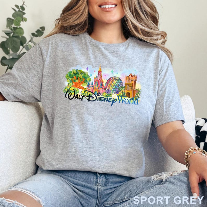 May include: A heather gray short-sleeve t-shirt featuring a colorful graphic print of the Walt Disney World theme park landmarks, including the Tree of Life, Cinderella Castle, Spaceship Earth, and the Tower of Terror, with the text Walt Disney World.