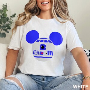 May include: White t-shirt featuring a blue and gray graphic of R2-D2 with Mickey Mouse ears. The design includes the number 18, a red square, and vertical blue lines. The word "WHITE" is printed at the bottom.