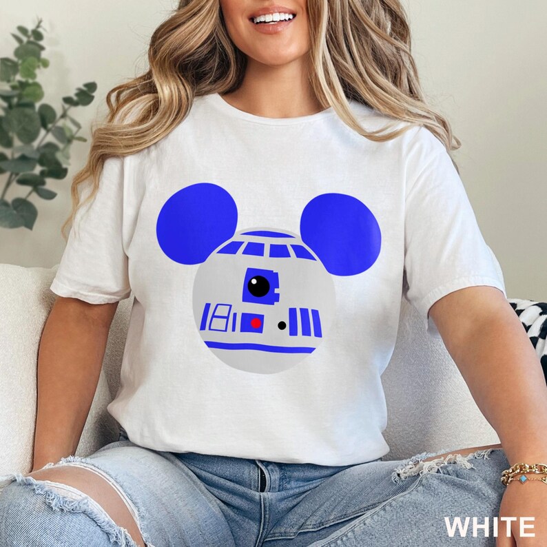 May include: White t-shirt featuring a blue and gray graphic of R2-D2 with Mickey Mouse ears. The design includes the number 18, a red square, and vertical blue lines. The word "WHITE" is printed at the bottom.