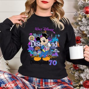 May include: Black sweatshirt featuring a colorful graphic of Mickey Mouse in front of Disneyland Resort imagery. The design includes the text "Walt Disney," "Disneyland Resort," and "Disneyland 70." The sweatshirt is a crew neck style.