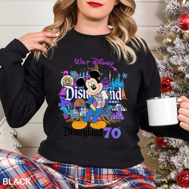 May include: Black sweatshirt featuring a colorful graphic of Mickey Mouse in front of Disneyland Resort imagery. The design includes the text "Walt Disney," "Disneyland Resort," and "Disneyland 70." The sweatshirt is a crew neck style.