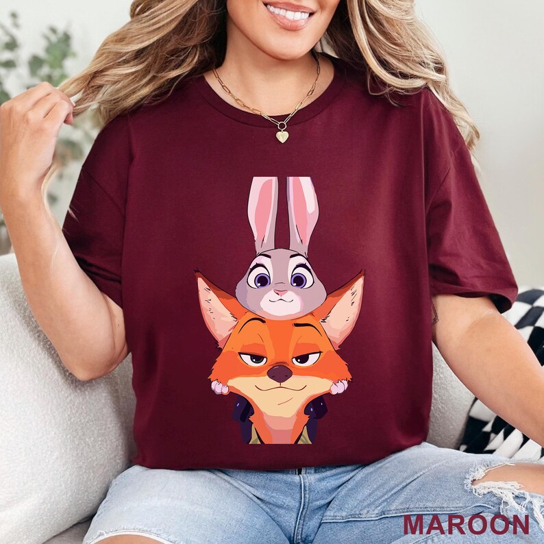 May include: Maroon t-shirt featuring a cartoon illustration of a fox and a rabbit. The fox is orange with a sly expression, and the rabbit is gray with long ears. The word "MAROON" is printed in white at the bottom right.