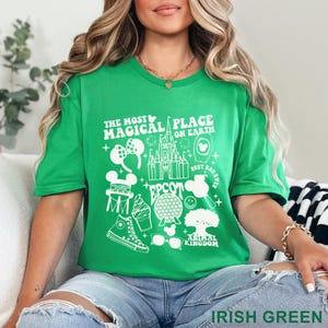 May include: Irish green t-shirt with a white graphic design featuring the text "THE MOST MAGICAL PLACE ON EARTH" and various Disney-themed icons, including a castle, Mickey Mouse ears, and a pair of sunglasses. The shirt is made of a soft material.