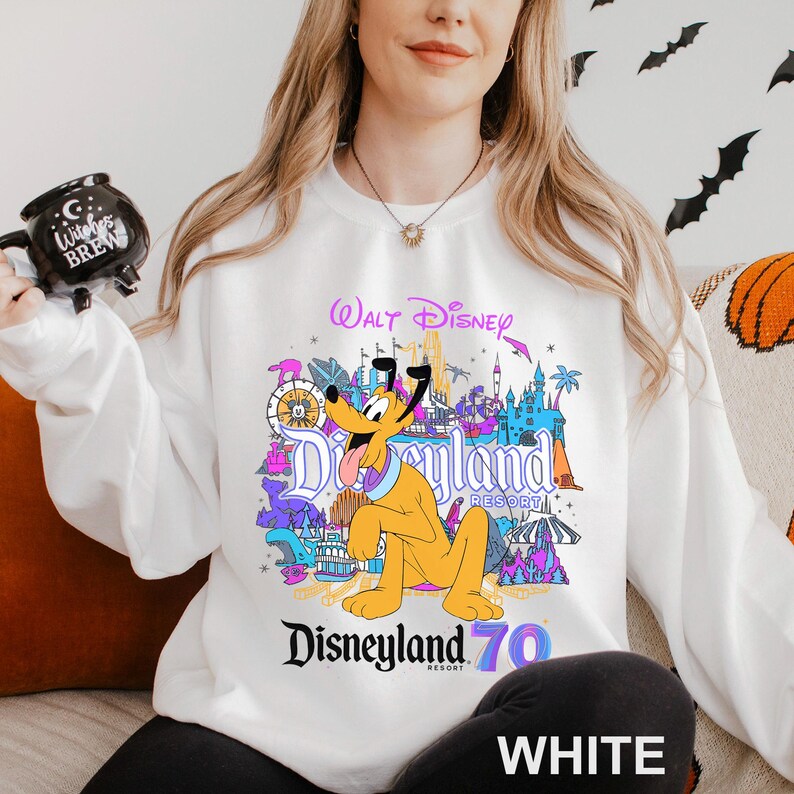 May include: White sweatshirt featuring a colorful Disneyland Resort graphic with Pluto. The design includes the text "Walt Disney" and "Disneyland Resort 70". The word "WHITE" is printed at the bottom of the sweatshirt.