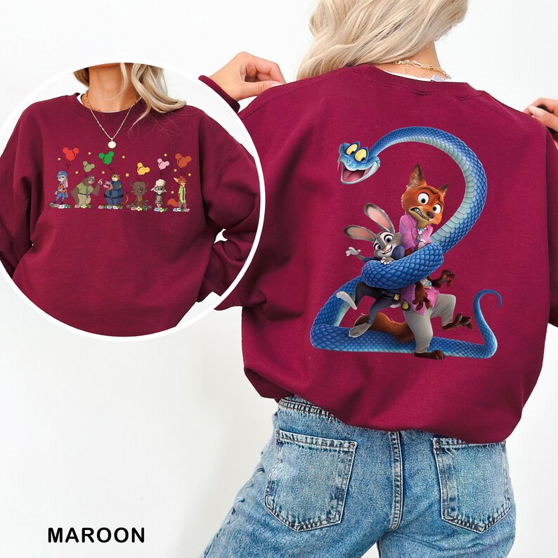 May include: A maroon crewneck sweatshirt featuring a large graphic on the back of a blue snake coiled around a fox and a rabbit. A circular inset shows the front of the sweatshirt with a smaller graphic of multiple characters holding balloons.