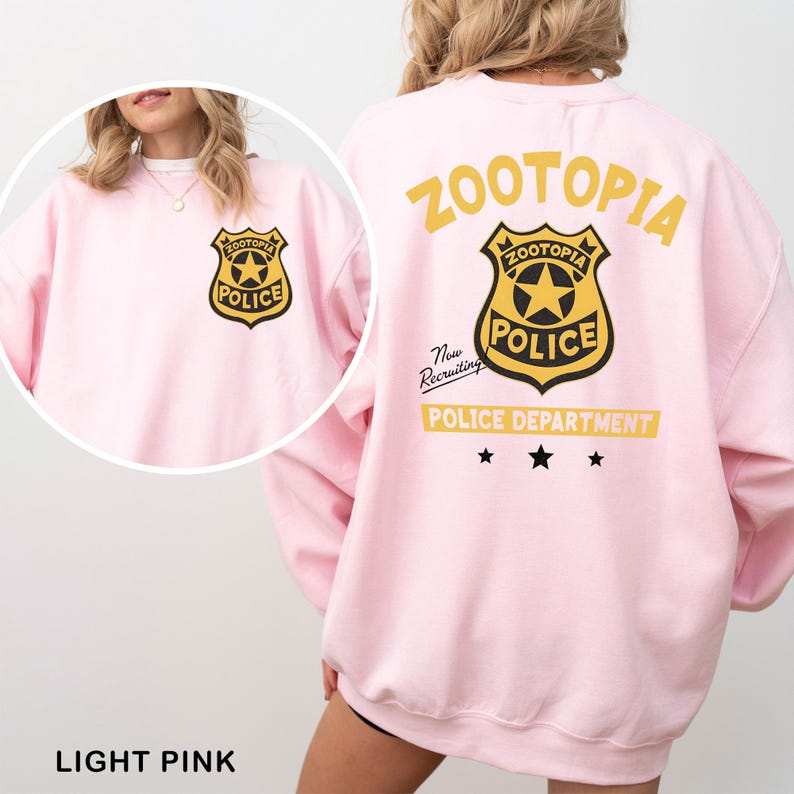 May include: Light pink sweatshirt featuring a Zootopia Police Department badge graphic on the front and back. The back design includes the word "Zootopia" above the badge, and "Police Department" below. The text "Now Recruiting" is also included.